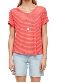 Femme portant un t-shirt rayé corail à manches courtes, un short en jean bleu clair et un collier pendentif rond.