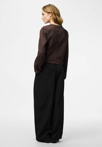 Brun cropped jakke med lange, oppustede ærmer, kombineret med løse sorte bukser. Glat tekstur; enkelt, minimalistisk design.