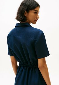 Abito camicia blu navy con maniche corte, colletto e vita stretta, caratterizzato da una texture liscia e un design minimalista.