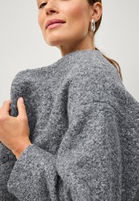 Maglione grigio texturizzato con una vestibilità ampia, realizzato in un materiale morbido e soffice e con colletto rotondo. L'indumento presenta un bottone sul polsino.
