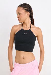 Black halter crop top with gathered neckline and flat hem, featuring a small white Nike logo on the chest. Model poses with pink shorts.