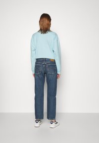 Sudadera azul de corte holgado, combinada con jeans azul clásicos de pierna recta con bolsillos traseros y un parche de la marca, usados con zapatillas blancas.
