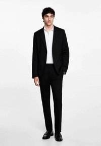 Costum negru croit, cu pantaloni drepți și sacou cu un singur nasture, asortat cu o cămașă albă. Țesătură netedă cu un design curat.