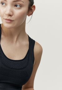 Musta urheilullinen hihaton paita, jossa on teksturoitu verkkopaneeli ja sileä kangas, leveät olkaimet ja pyöreä pääntie.