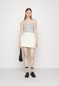 Top de rayas sin mangas con botones, combinado con una minifalda blanca plisada. Los accesorios incluyen un bolso negro y calcetas con patrón de corazones junto con zapatos.