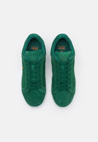 Gröna mockaskor med platta snören och vadderad krage. Har en logotyp i orange på tungan och en vit gummisula.