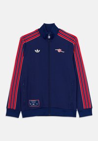 Mörkblå jacka med röda ränder, dragkedjestängning, hög krage, Adidas-logotyp på bröstet och Arsenal-kanonemblem. Har en sidoficka med dragkedja.