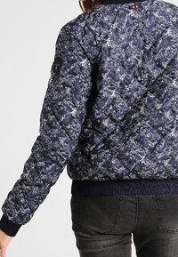 Marineblauer gesteppter Bomberjacke mit einem weißen Blumenmuster, gerippten Bündchen und Saum sowie einem Logo-Patch auf dem linken Ärmel.