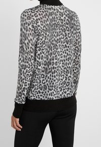 Szary i czarny sweter w panterkę z długimi rękawami, czarnymi prążkowanymi mankietami i dołem oraz lekko luźnym krojem. Lekki, teksturowany materiał.