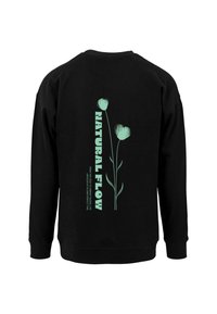 Sort sweatshirt med et grønt blomstermotiv og teksten "NATURAL FLOW" på ryggen. Fremstillet af blødt stof med ribbede manchetter.