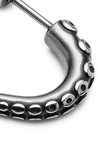 Sølvfarvet metalørering formet som en blækspruttearm, med struktureret overflade og runde sugekopper langs kanten.