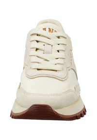 Beige und cremefarbene Sneakers mit dicker brauner Sohle, abgerundetem Zehenbereich, Wildleder- und Stoffpaneelen sowie beige Schnürsenkeln, die kreuzweise gebunden sind.
