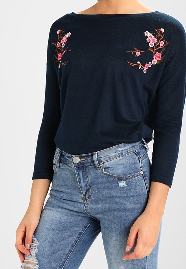 Marineblauw long-sleeve shirt met geborduurde roze bloemenpatronen op de borst, gecombineerd met lichtblauwe distressed skinny jeans.