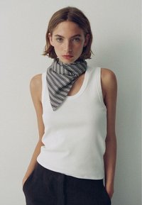 Hvid ribbet tanktop parret med et sort-hvidt stribet tørklæde knyttet om halsen, sat mod en neutral baggrund.