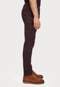 Bordowe spodnie o dopasowanym kroju wykonane z teksturowanej tkaniny, z kieszenią na zamek błyskawiczny. W zestawie z brązowymi sznurowanymi botkami zamszowymi.