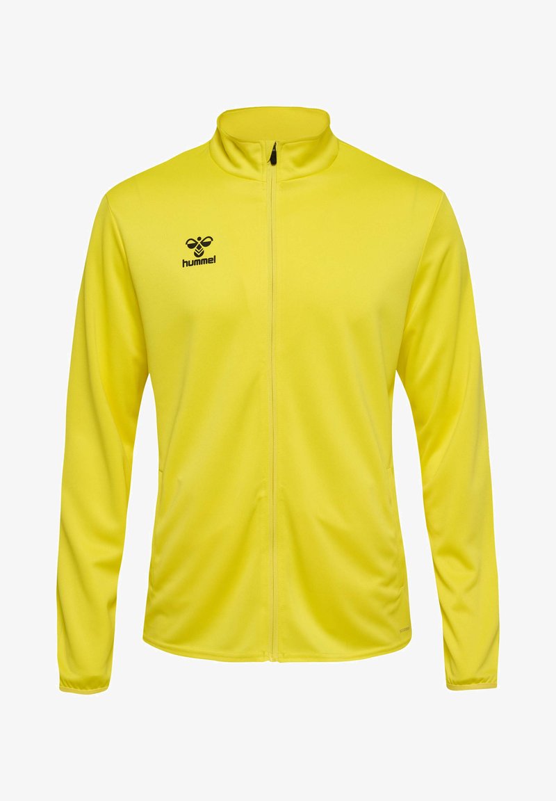 Gul lynlåsjakke lavet af glat, let materiale. Har en opretstående krave, lange ærmer og sort logo på den øverste venstre side.