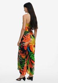 Mono multicolor con corsé fruncido, que presenta grandes estampados de hojas tropicales y flores en naranja, verde y negro, con patas anchas.