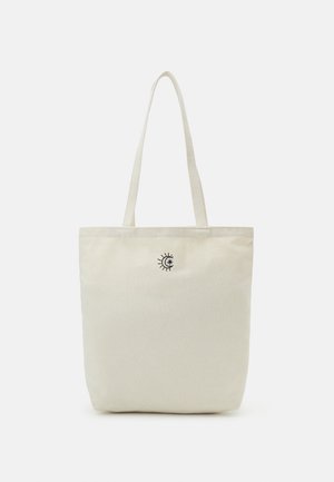 Beige canvas tote bag with long handles and small black sun and moon design centered near the top.
