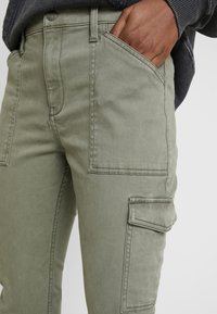 Cargo-byxor i olivgrön, tillverkade av bomullsblandning. Har flera fickor, strukturerad sömnad och mjuk textur.
