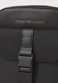 Schwarzer Leder-Rucksack mit strukturierter Oberfläche, ausgestattet mit einem Riegelverschluss und geprägtem "TOMMY HILFIGER"-Logo auf der Vorderseite.