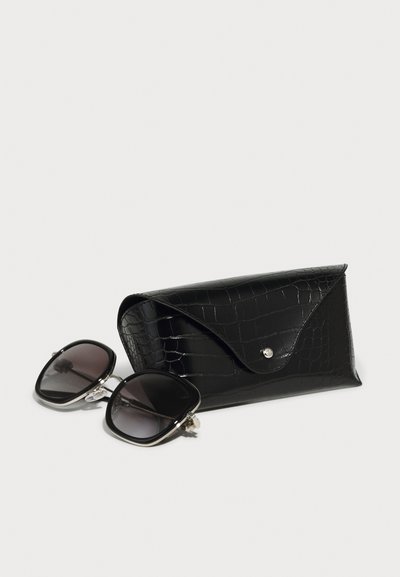 Etui pentru ochelari de soare, de culoare neagră, cu imprimare crocodil și închidere tip clemă, alături de ochelari de soare mari, pătrați, cu lentile întunecate cu gradient și accente argintii.
