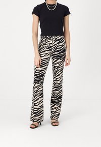 Black short-sleeve top paired with zebra-print flared pants in cream and black, with a smooth texture and minimalistic heeled sandals.