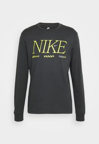 Schwarzes Langarm-T-Shirt mit gelbem Nike-Logo und weißen Akzenten. Verfügt über einen Rundhalsausschnitt und gerippte Bündchen, gefertigt aus weichem Baumwollstoff.