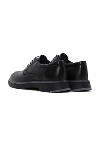Zapatos de cuero negro con forma redondeada, textura suave y suela de goma contrastante con un acento gris. Diseño con cordones y un detalle mínimo.