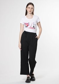 Camiseta blanca con un gráfico colorido de "AMOR", combinada con pantalones anchos negros, que tienen una cintura elástica y bolsillos laterales. Zapatos negros sin cordones.