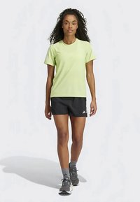 Lima zaļš sporta krekls ar īsām piedurknēm, apvienots ar melniem šortiem, kuriem ir akcenta logs. Modelis valkā pelēkas zeķes un sportiskus apavus.