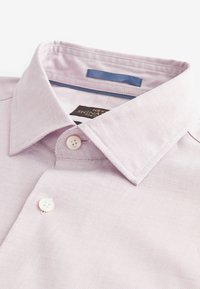 Heled lilla särk, millel on tekstuuriga muster, nööpidega krae ja kaks valget nööpi ees. Sildil on kirjas "NEXT SIGNATURE, 100% puuvill."
