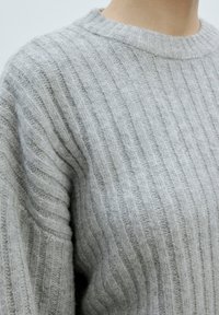 Grau gestrickter Pullover mit gerippter Textur, runder Ausschnitt und lockerer Passform. Nahaufnahme, die die detaillierte Naht zeigt.