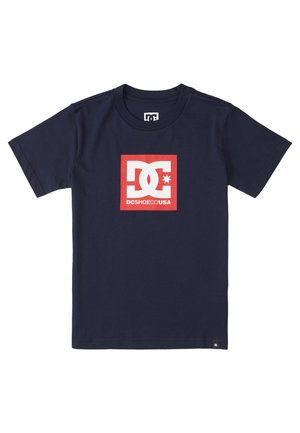 Marineblå t-shirt med korte ærmer, med en rød firkantet logo, der viser hvide sammenflettede "DC"-bogstaver og teksten "DCSHOECOUSA".
