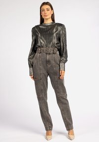 Metallic zwarte blouse met lange mouwen en een hoge hals, gecombineerd met hooggetailleerde grijze denimbroek met een riem en zijzakken.