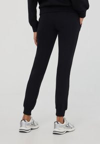 Pantaloni sportivi neri con silhouette aderente, cintura elastica e polsini alle caviglie, abbinati a scarpe sportive argentate.