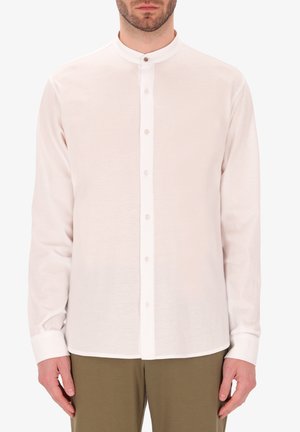 Camicetta rosa chiaro a maniche lunghe con colletto a bande, patta dei bottoni frontale e texture liscia. Abbinata a pantaloni verde oliva.