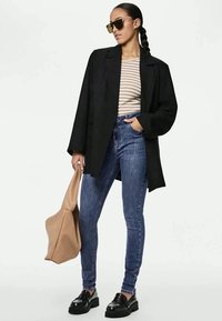 Fekete oversized blézer, csíkos hosszú ujjú felső, kék skinny farmere, fekete loafers, és barna tote táska. A napszemüveg teszi teljessé az összeállítást.
