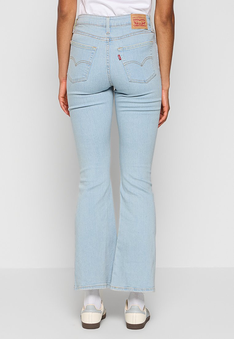 Hellblaue Schlagjeans aus Denim-Stoff mit hoher Taille, ausgestattet mit Gesäßtaschen und einem markierten Lederpatch auf der Rückseite.