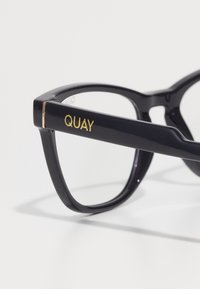 Mustat suorakulmaiset lasit kiiltävällä pinnalla. Ominaisuuksia kultainen "QUAY" -logo varressa. Sileä rakenne ja tukeva design.