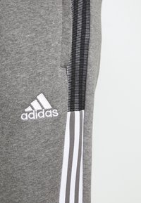Grijze joggingbroek met een zwart mesh-streep aan de zijkant, wit Adidas-logo en contrasterende witte en grijze strepen op het onderbeen.
