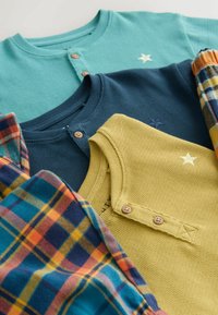 Tre strikkede bluser i teal, marineblå og gul, med rund hals, knapper og stjernebroderi. Inkluderer et stof med ternet mønster.