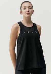 Svart atletisk linne med en genomskinlig meshpanel vid halsringningen och subtila grafiska mönster framtill. Design med spagettiband.