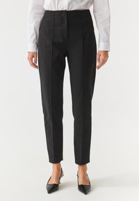 Zwart op maat gemaakte broek met een hoge taille, voorzien van voorplooien en een slim fit. Het materiaal heeft een gladde textuur, gecombineerd met spitse zwarte hakken.