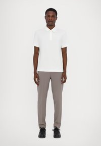 Hvit kortermet polo-skjorte med krage, kombinert med lysegrå bukser og svarte sko. Glatt tekstur, minimalistisk design.