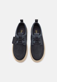 Navy suede shoes with a contrasting light outsole, featuring a rounded toe and lace-up design with visible stitching and a logo tag.