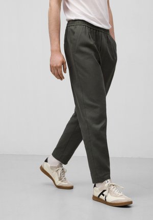 Olive green elastic waistband pants with side pockets, paired with beige and black sneakers, featuring cream laces and a rubber sole.