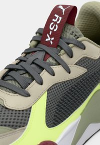 Sport sneaker with gray mesh and beige synthetic upper, featuring a neon green accent and red lace loop. Textured patterns throughout.