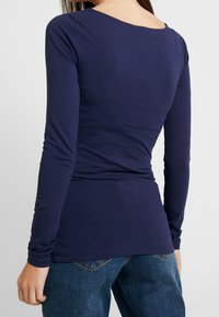 Mörkblå långärmad topp i ett mjukt, stretchigt tyg med rundad urringning och figursydd siluett, kombinerad med midjehöga blå denimjeans.