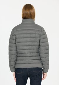 Graue isolierte Jacke mit horizontalem Steppmuster, hohem Kragen und elastischen Bündchen, kombiniert mit dunkelblauen Jeans. Glatte, glänzende Textur.