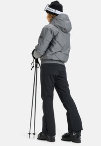Giacca a vento grigia con cappuccio, pantaloni da sci neri, bastoni da sci e stivaletti da neve. Gli accessori includono un berretto nero con logo.